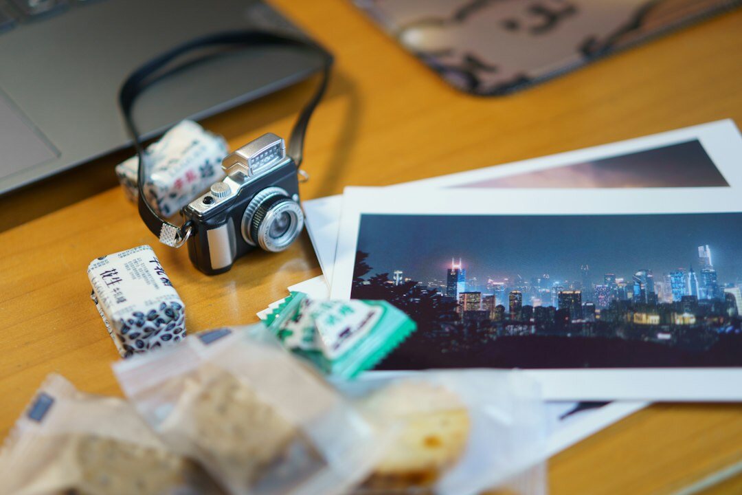 Hands editing black and white photographs on a laptop with printed contact sheets on a wooden desk